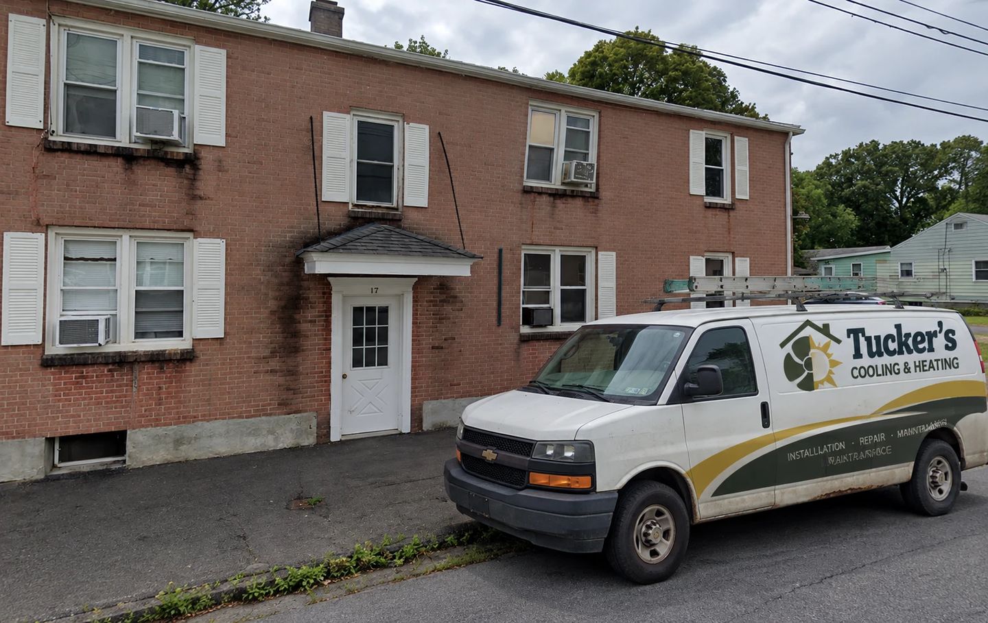Tucker’s Cooling & Heating service van parked outside a brick apartment building in Rensselaer